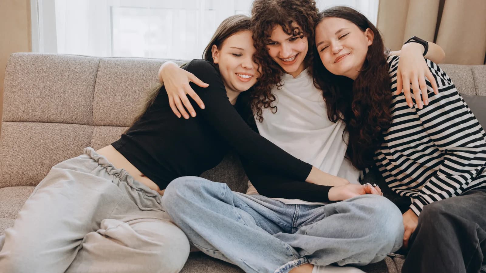 Teen sisters embracing on a sofa for an article about siblings and teen mental health