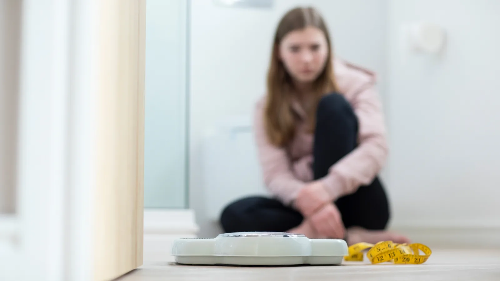 Teen girl sitting near a scale and measuring tape for an eating disorder warning signs guide