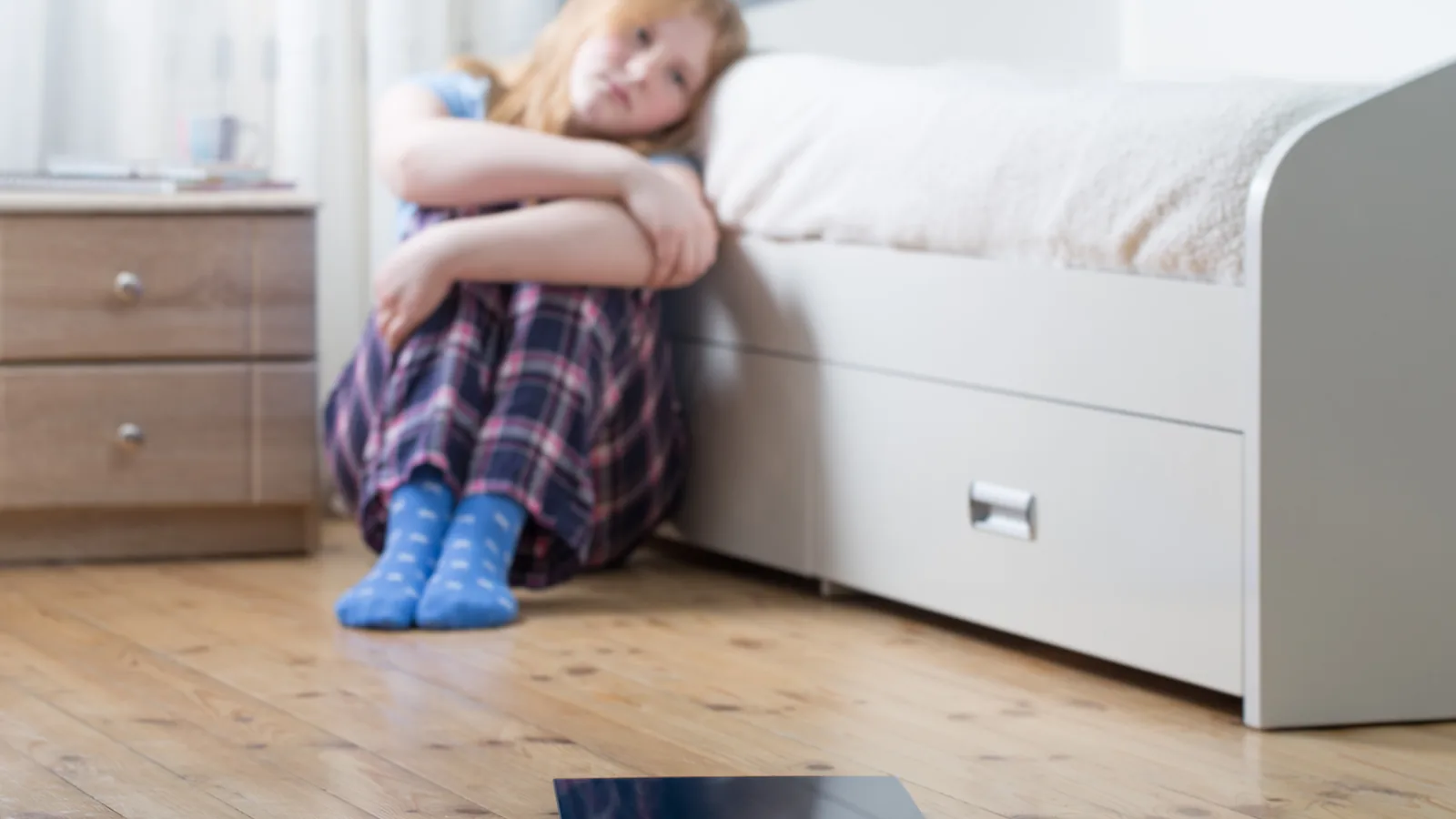 Sad teen girl sitting on the floor near a bathroom scale for an eating disorder warning signs guide