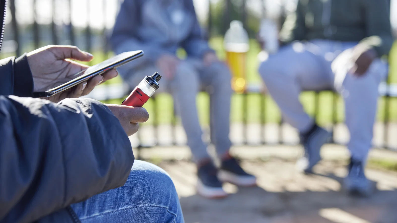 Teen holding a vape device near other teens outdoors for a parent guide about vaping and THC